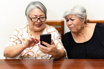 A photo of a female audiologist providing a hearing aid consultation to a middle-aged male client with brown skin and a beard.