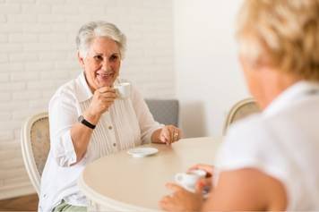 A photo of an older woman with silver hair taking a hearing assessment in a soundproof booth while an audiologist monitors the results.